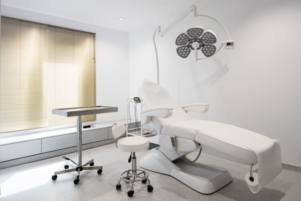 Sală de tratament din clinica Wanderma, Craiova: pat de procedură, lampă chirurgicală și masă cu instrumentar.